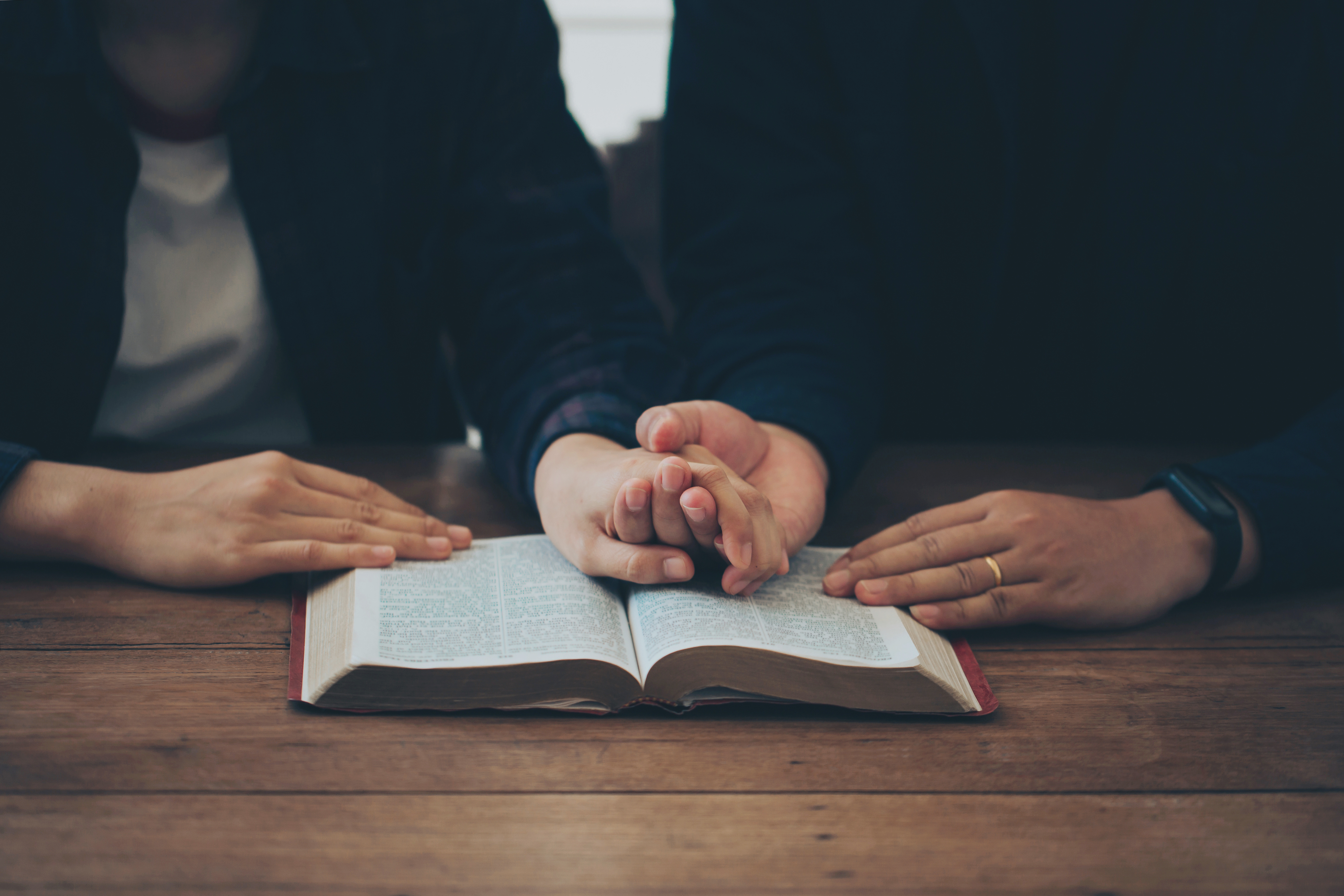 Couple holds hands over the Bible while praying for marriage guidance.