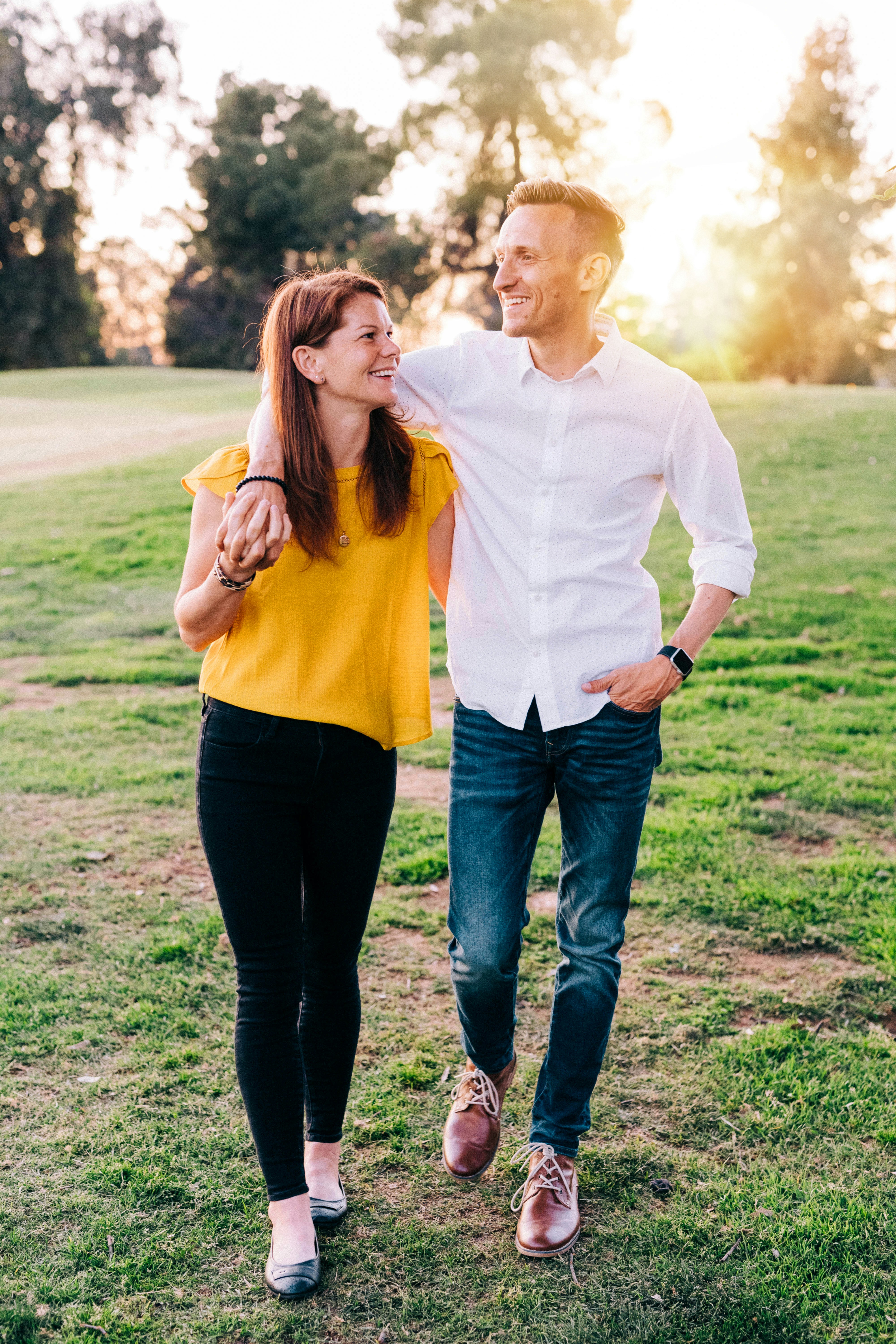 A smiling husband and wife walking arm-in-arm through a grassy park at sunset, demonstrating the joy of intentional pursuit and building a healthy, strong Christian marriage.