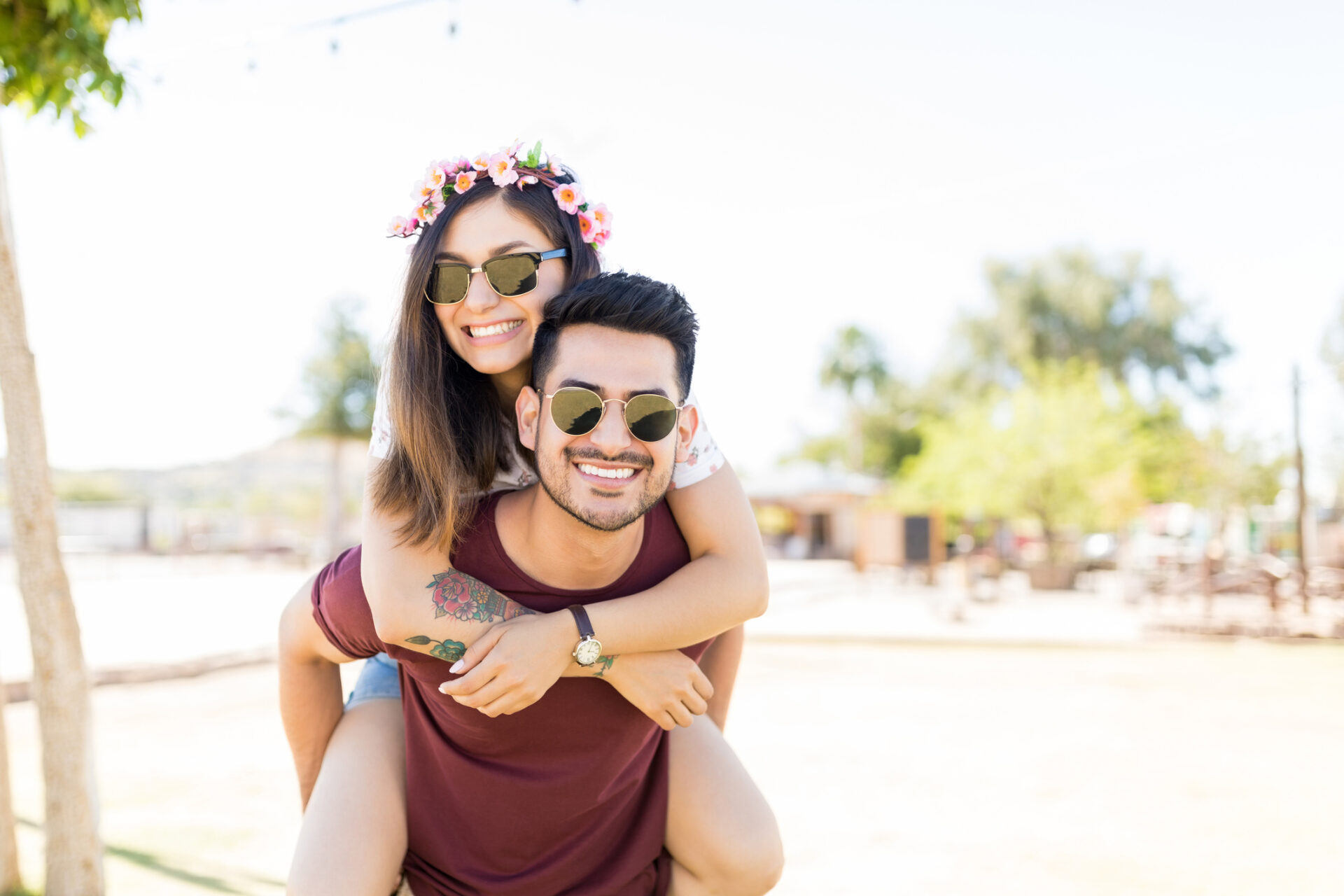 Portrait of good looking couple wearing sunglasses while enjoying piggyback ride at music festival