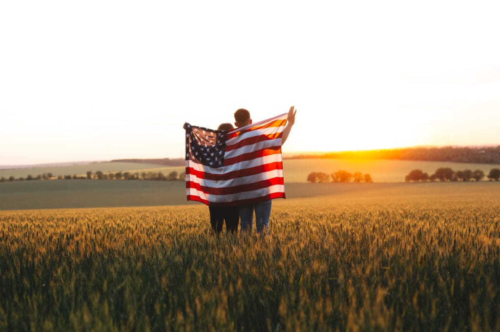 couple in a field holding an american flag behind them