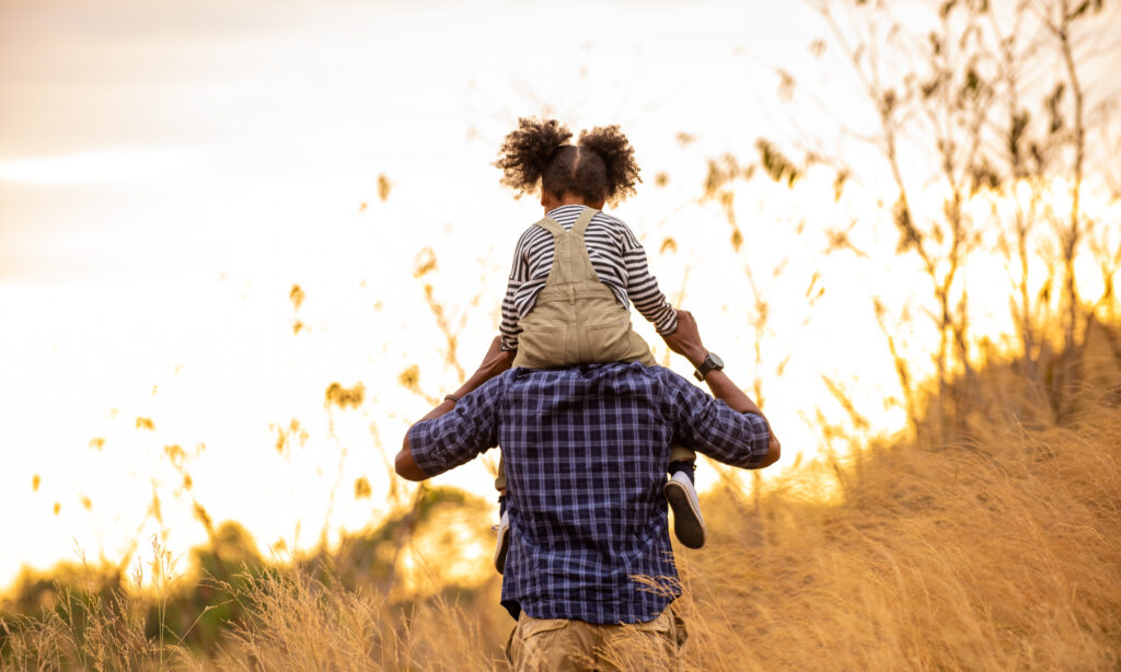 a father with his daughter on his sholders in a field