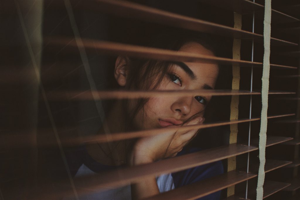 woman looking through blinds out a window