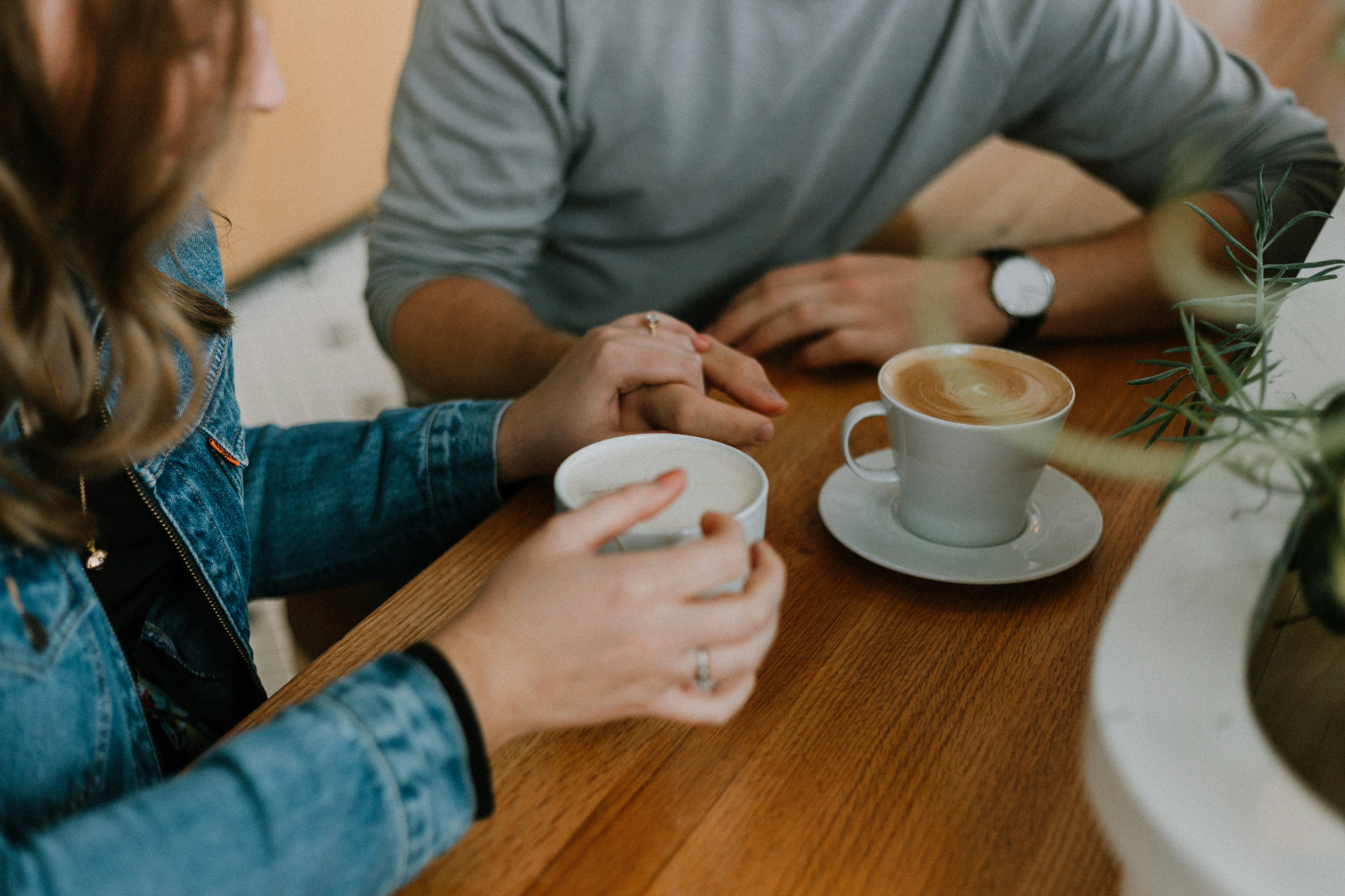 A married couple holding hands over coffee cups on a wooden table, representing quality time, healthy communication, and intentional pursuit in marriage.