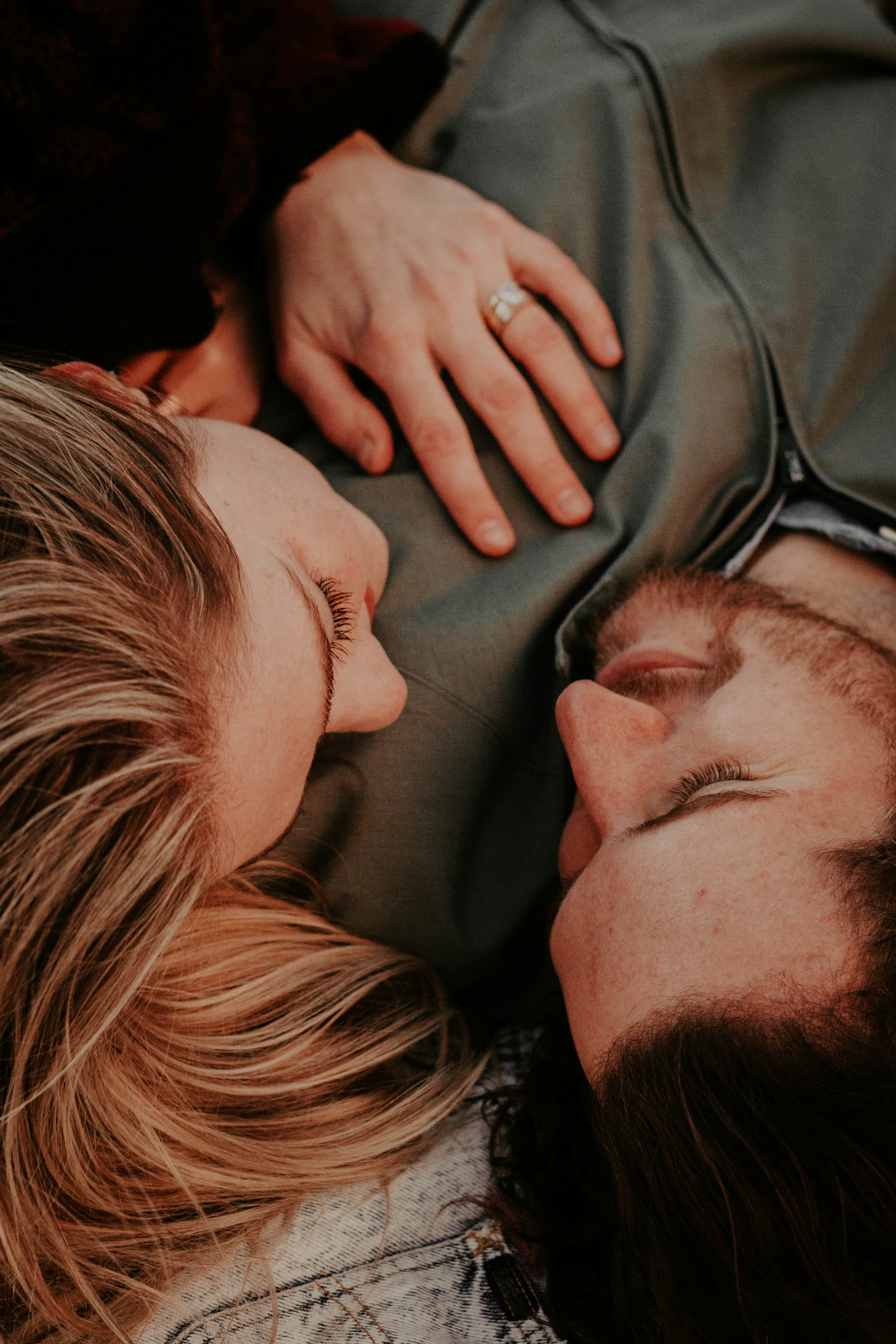 Overhead view of a young husband and wife lying down close together, looking into each other's eyes with her hand resting on his chest, representing how to romance your spouse and build deep connection.