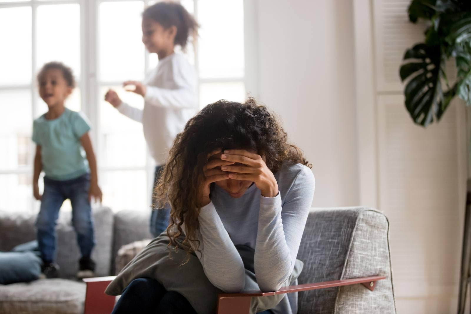 a woman stressed with her head in her hands while kids are behind her