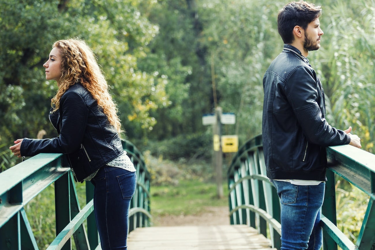 couple on a bridge on opposite sides looking away from eachother